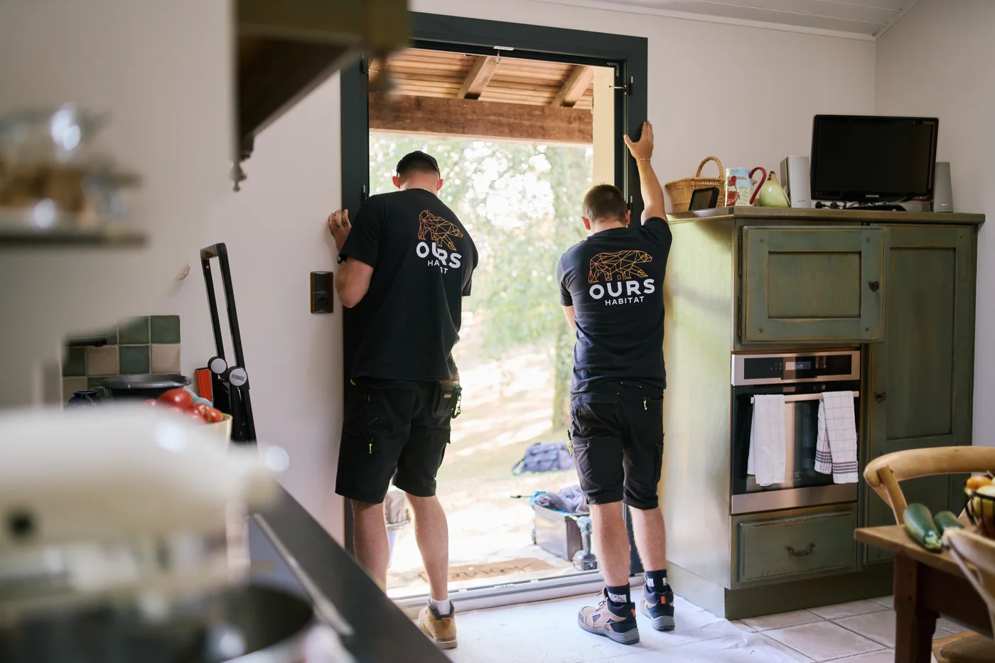 Deux artisans Ours Habitat installent une baie dans une maison