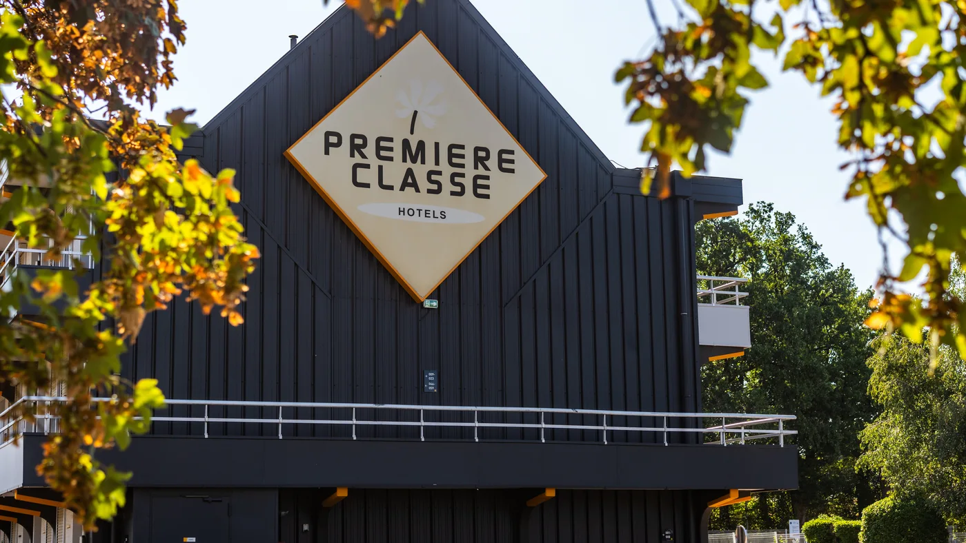 Façade d’un hôtel Première Classe photographiée à travers les feuillages